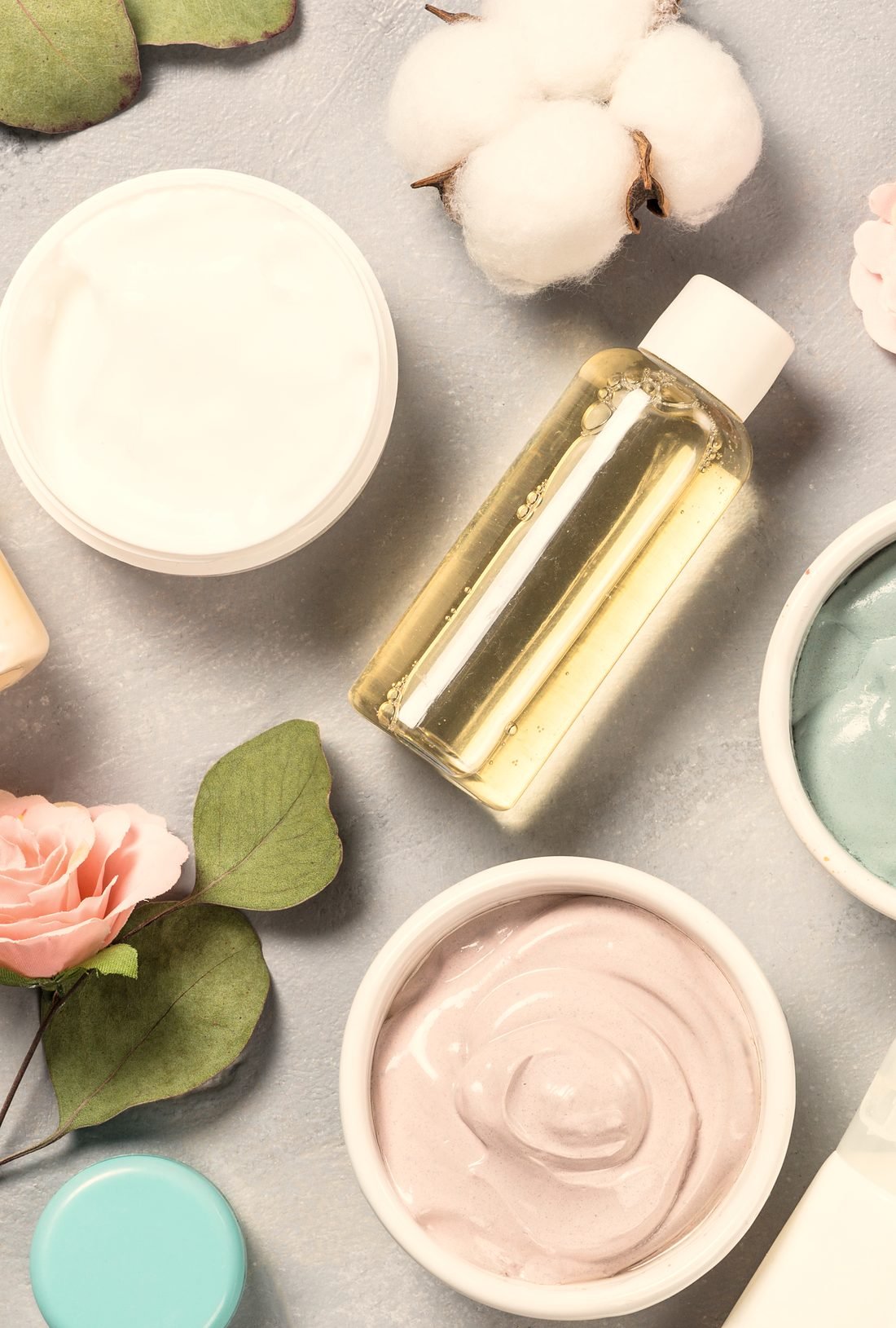 Creams, oils and bottles arranged with roses and eucalyptus