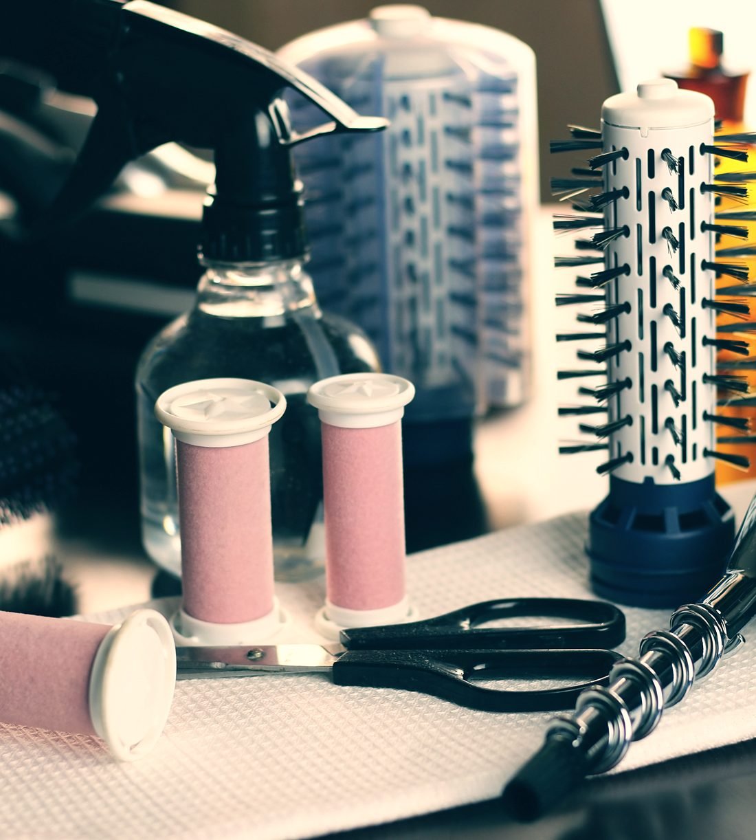 Hair rollers, round brushes, scissors and a spray bottle on a salon station
