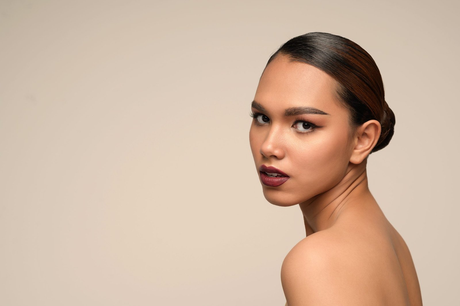 Portrait of a woman with sleek hair and a deep berry lip against a warm beige backdrop